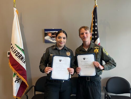 Two people holding papers in front of a flag.