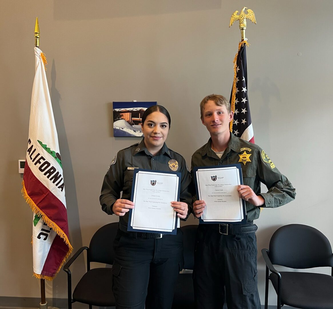 Two people holding papers in front of a flag.